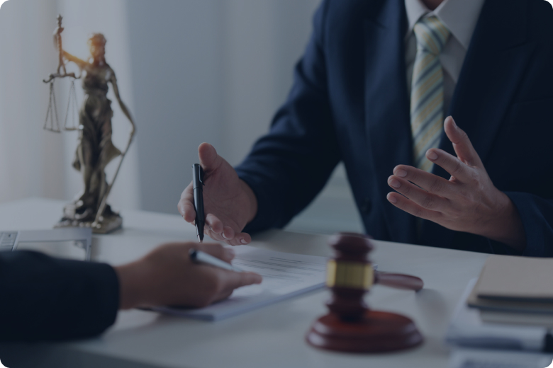 Lawyer in a suit signs papers at a desk, gavel and scales statue visible in the background, symbolizing justice.